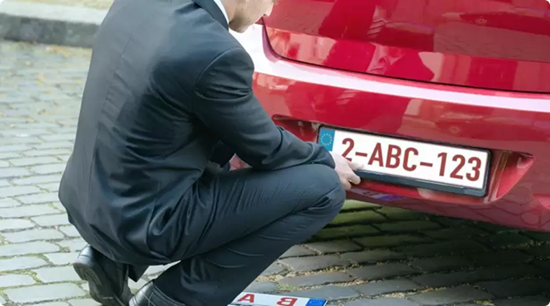 Crouching man at the license plate at the rear of a car