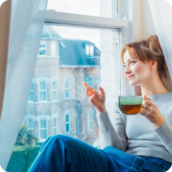 vrouw die thee drinkt bij haar raam